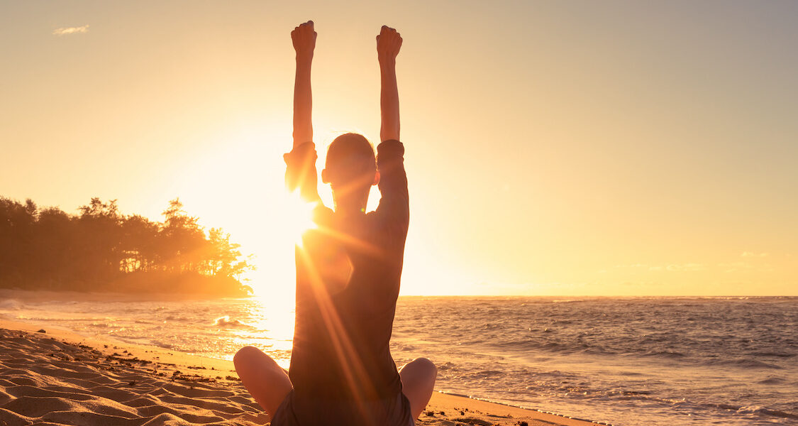 young woman sitting on a beach feeling strong inspired energized facing the sunrise young woman sitting on a beach feeling strong inspired energized facing the sunrise